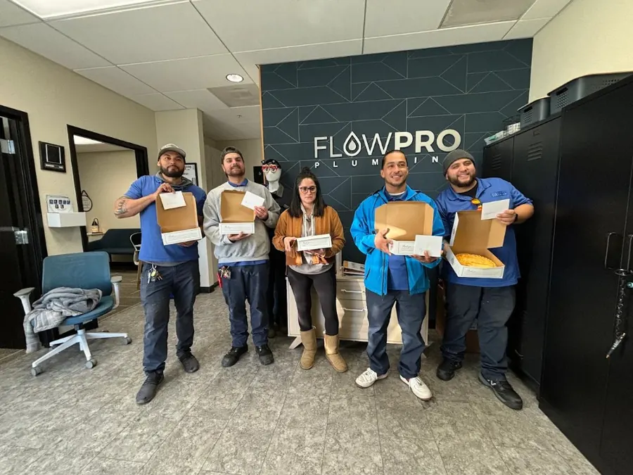 The Flow Pro Plumbing team gathered in the company office in front of the Flow Pro logo wall