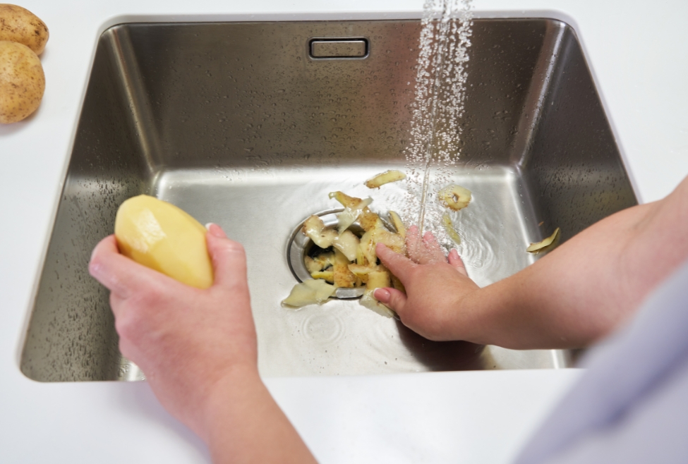 Home Potato peels being rinsed into a kitchen sink drain, illustrating why you shouldn't put food in garbage disposal to avoid clogs, damaged blades, and the need for professional garbage disposal repair by Flow Pro Plumbing. Trust us to help you with why you shouldn't put food in garbage disposal, can you put food scraps in garbage disposal, what not to put in a garbage disposal, garbage disposal clog repair, garbage disposal not working, garbage disposal maintenance tips, food waste in garbage disposal problems, kitchen drain clog removal, garbage disposal repair near me, garbage disposal installation near me, professional plumbing services for kitchen drains, local plumber for garbage disposal issues, Brentwood garbage disposal repair, Flow Pro Plumbing garbage disposal services, garbage disposal cleaning near me, best way to clean a garbage disposal, food stuck in garbage disposal, sink backup garbage disposal, garbage disposal leaking from bottom, clogged kitchen sink near me, garbage disposal jammed fix, garbage disposal troubleshooting, garbage disposal blade damage, plumbing services near me.