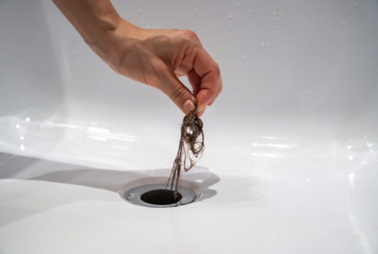 Hand pulling hair from a clogged bathtub drain, showing a common plumbing issue caused by hair buildup. Flow Pro Plumbing provides professional bathtub drain cleaning, hair clog removal, and clogged drain services for homeowners searching how to unclog bathtub full of hair. Contact us today for help with how to unclog bathtub full of hair, bathtub drain clogged with hair, best way to remove hair from bathtub drain, unclog bathtub drain hair removal, clogged tub drain fix, hair clog in bathtub drain, drain cleaning near me, bathtub plumbing repair, professional drain unclogging service, Flow Pro Plumbing hair clog removal, slow bathtub drain fix, emergency plumber for clogged tub, drain cleaning services near me, plumber to unclog bathtub, hydro jetting services near me, drain snaking service near me, tub drain backed up with hair, affordable bathtub drain repair, shower drain hair removal, local plumbing services for clogged drains.